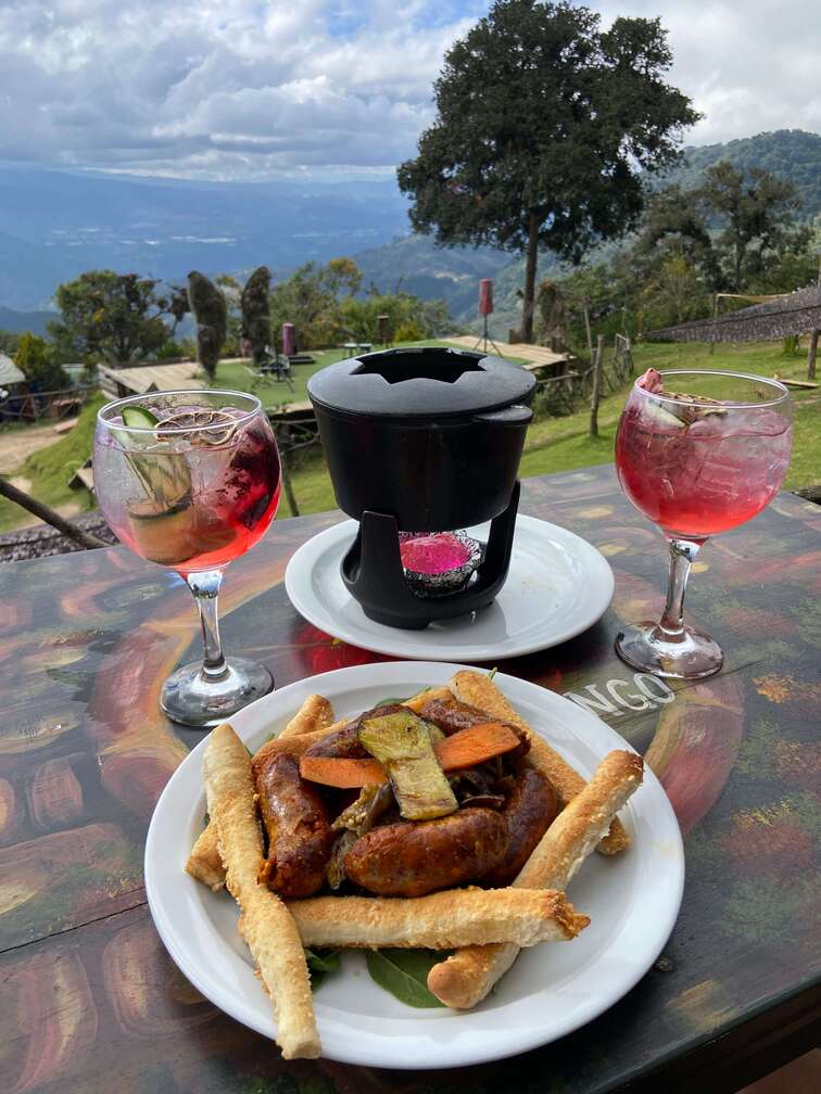 Cheese fondue and pink cocktails in Hobbitenango with the mountains in the background.